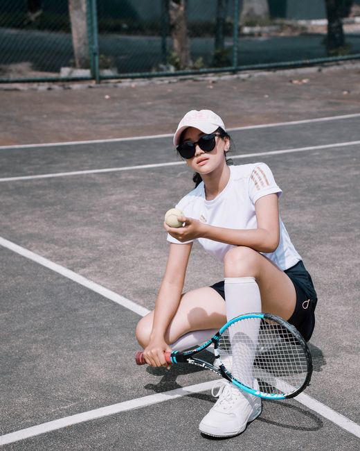 Woman sitting on a tennis court holding a tennis ball and racket, Bandung, Indonesia.