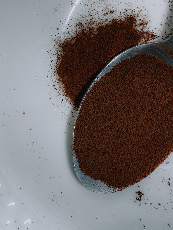 Ground coffee powder in teaspoon on white surface