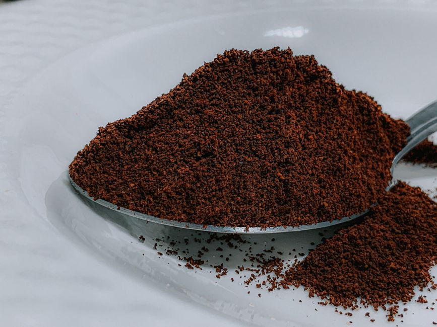 Closeup aromatic organic ground coffee heaped in silver teaspoon on white ceramic plate on table in cafeteria kitchen