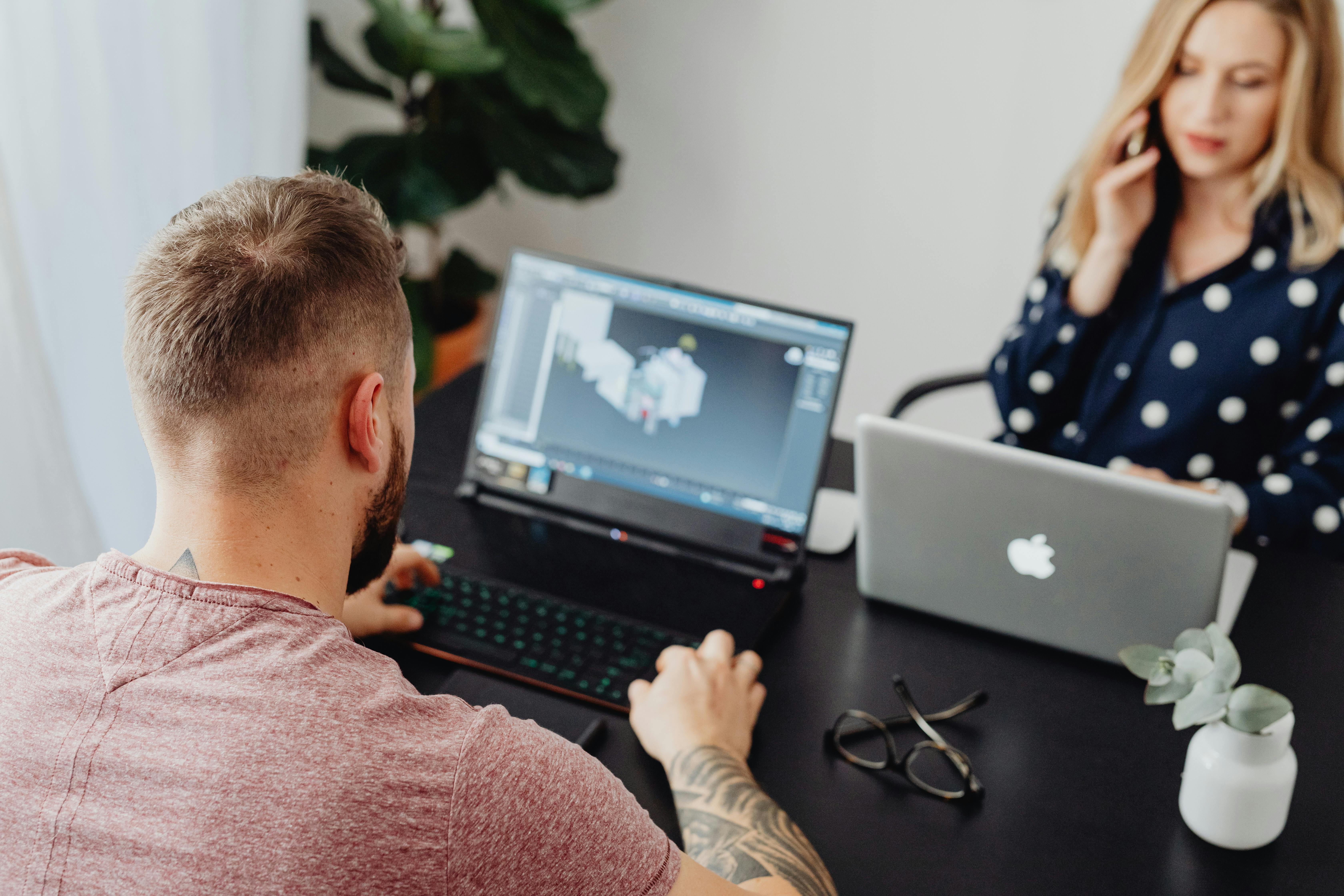 Two professionals working on laptops, engaging in a collaborative office environment.