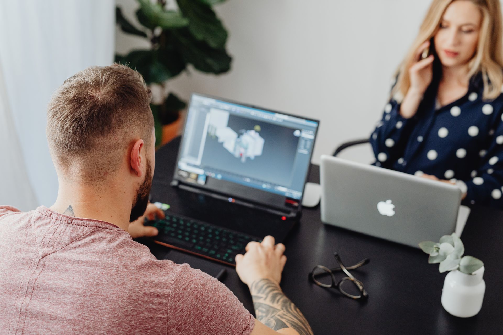 Two professionals working on laptops, engaging in a collaborative office environment.