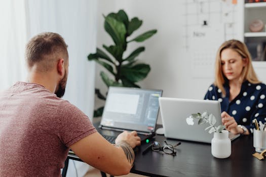 Two coworkers using laptops in a modern office setting, focusing on collaborative work.
