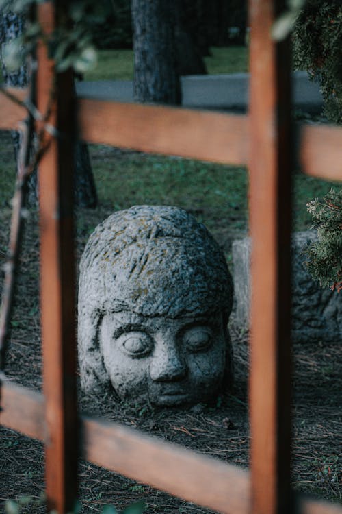 City park with wooden fence and old stone human head