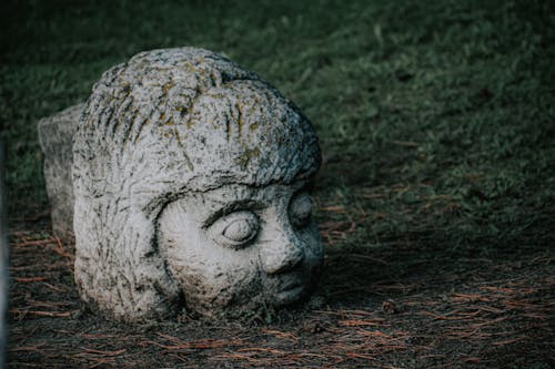 Massive shabby gray concrete part of sculpture located near grassy field on dry land with coniferous needles