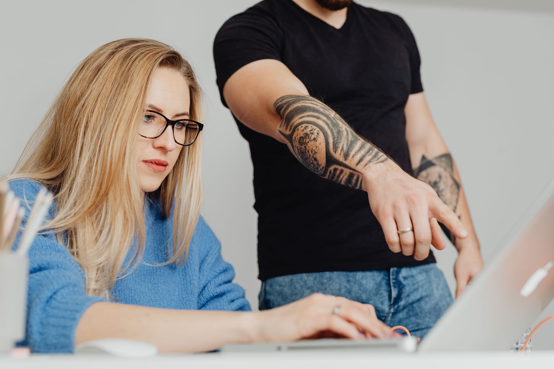 Woman working on a laptop with a man pointing, showing teamwork in action.