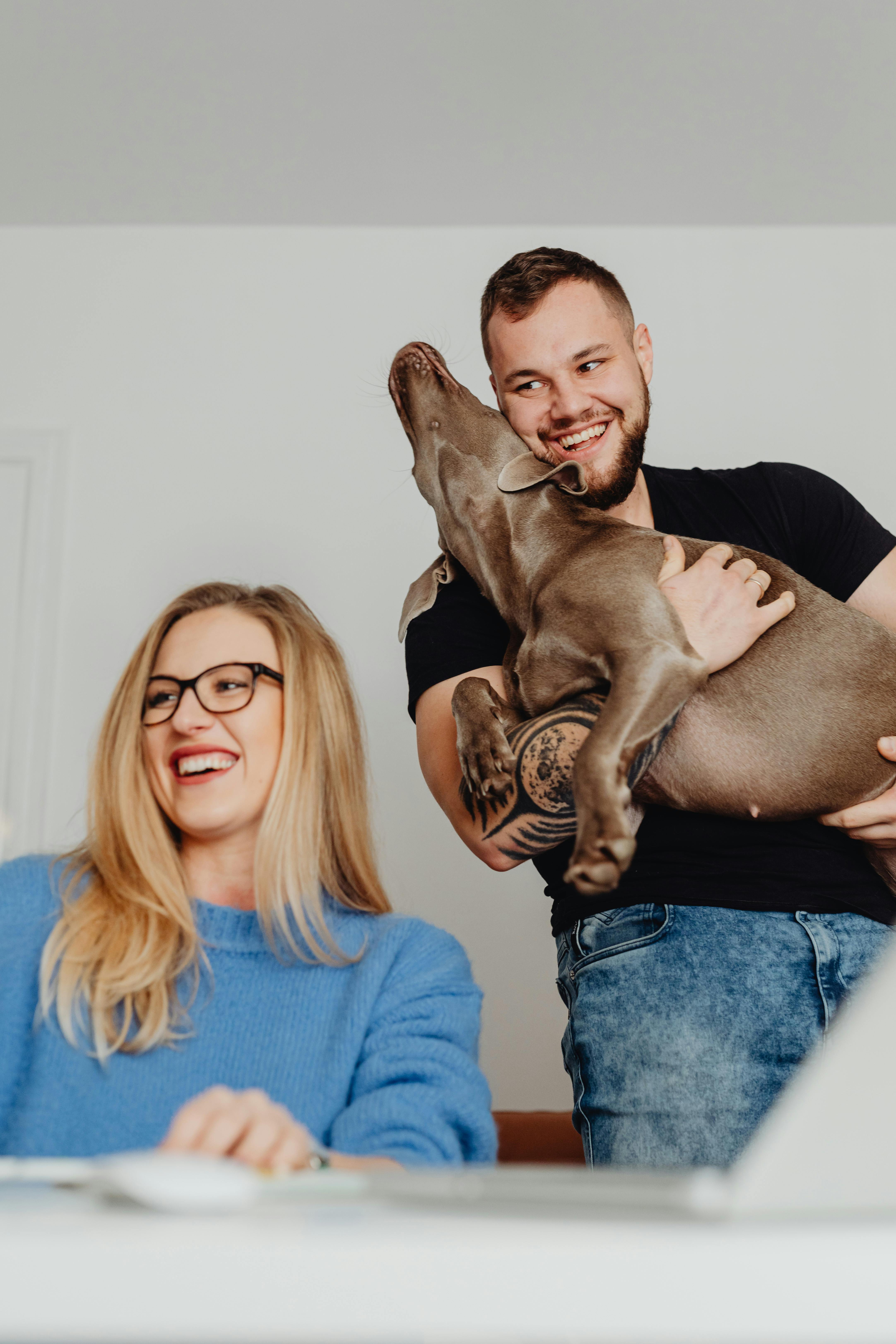 Smiling couple enjoying playful moments with their dog indoors. Bright and cheerful atmosphere.