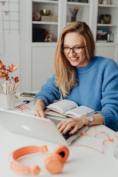 A cheerful woman in a blue sweater working remotely with a laptop in a cozy home setting.