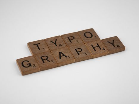 Wooden Scrabble tiles arranged to spell 'Typography' on a white surface.