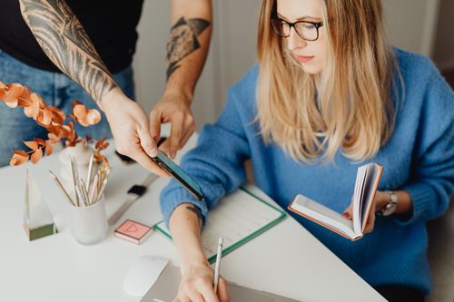 Free Woman in blue sweater working at home with a notebook, being assisted by a colleague. Stock Photo
