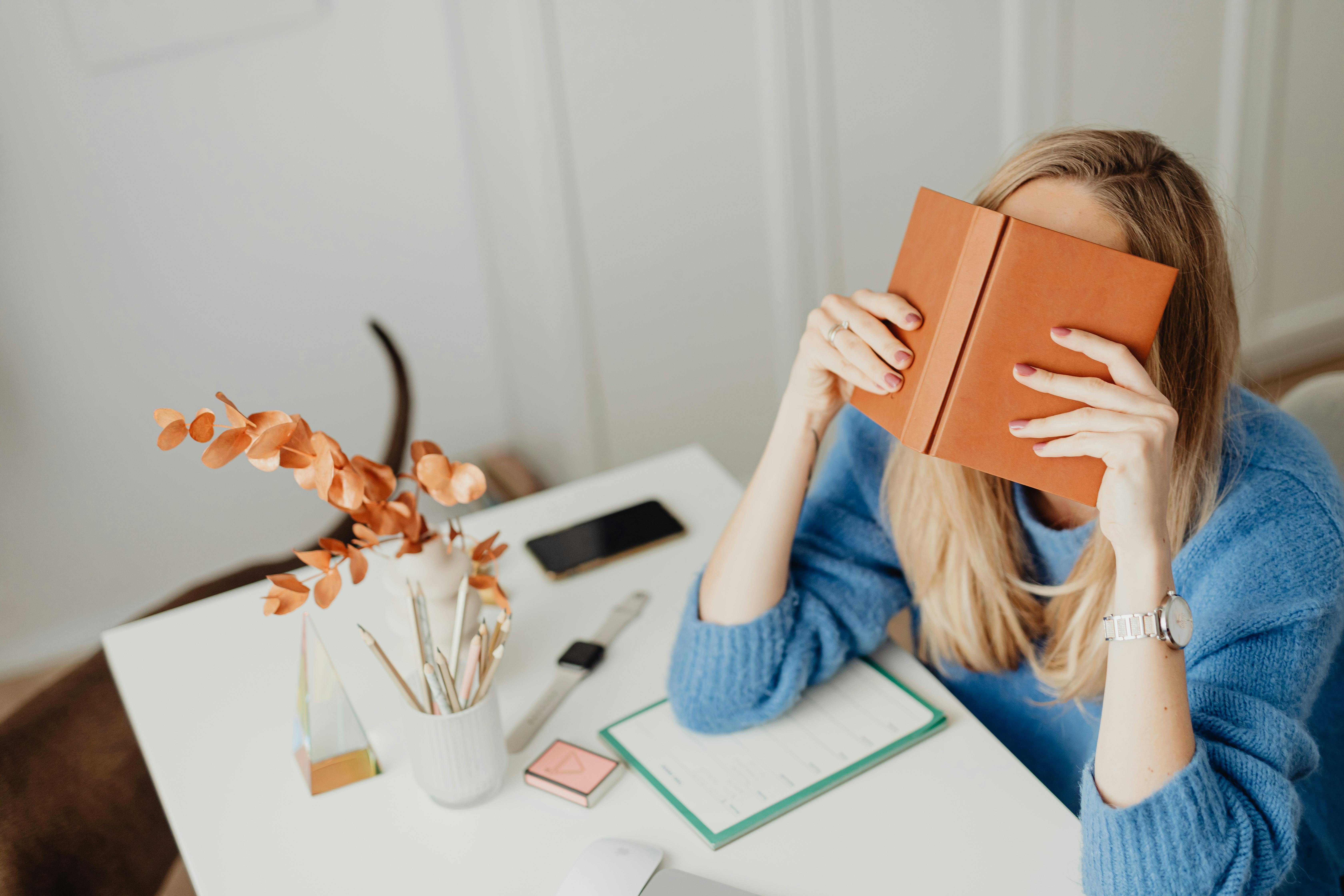 Woman in Blue Sweater Holding a Book on Her Face · Free Stock Photo