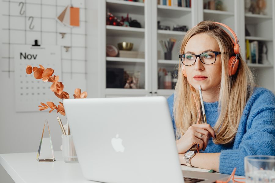 Blonde woman with headphones, working thoughtfully at home with a laptop.