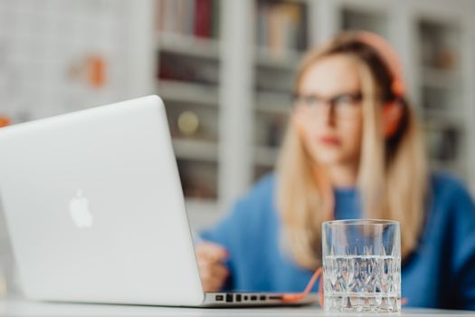 Focused woman working on laptop with a glass of water in the foreground. Indoor setting.