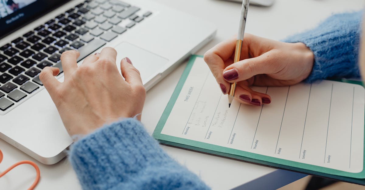 Person writing in planner while using laptop for time management