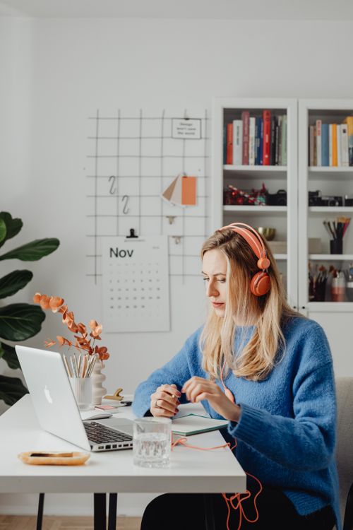 Free Adult woman in blue sweater using laptop at home office with plants and calendar in view. Stock Photo