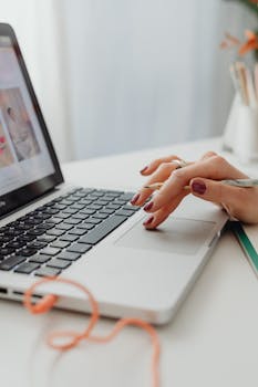 Woman's hand with manicured nails using a laptop touchpad, demonstrating attention to style.