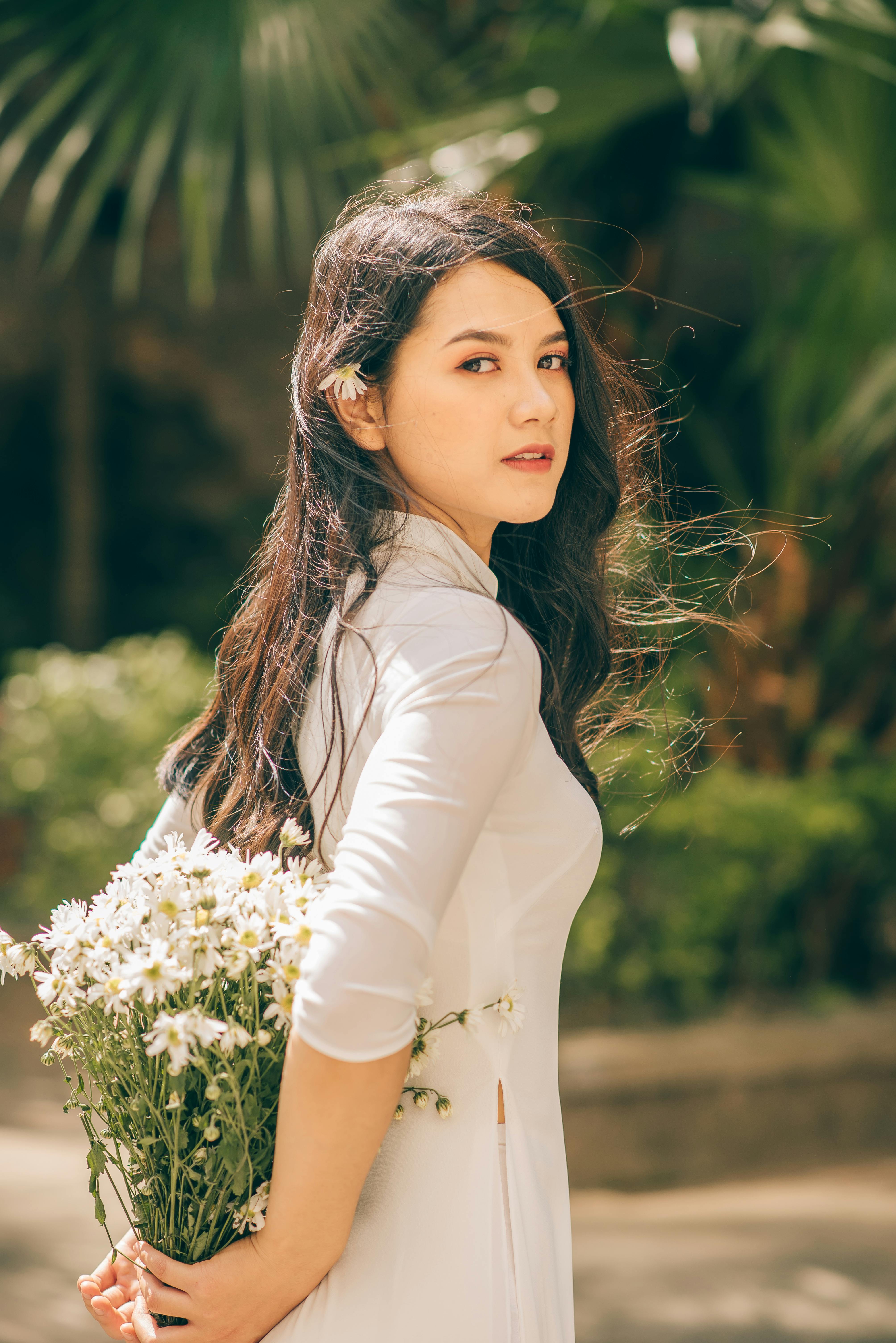 Portrait of an elegant woman holding a bouquet of daisies outdoors on a sunny day.