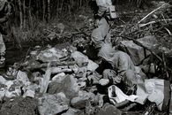 Black and white of anonymous male scientists with hammer among rough rocky formations against woods
