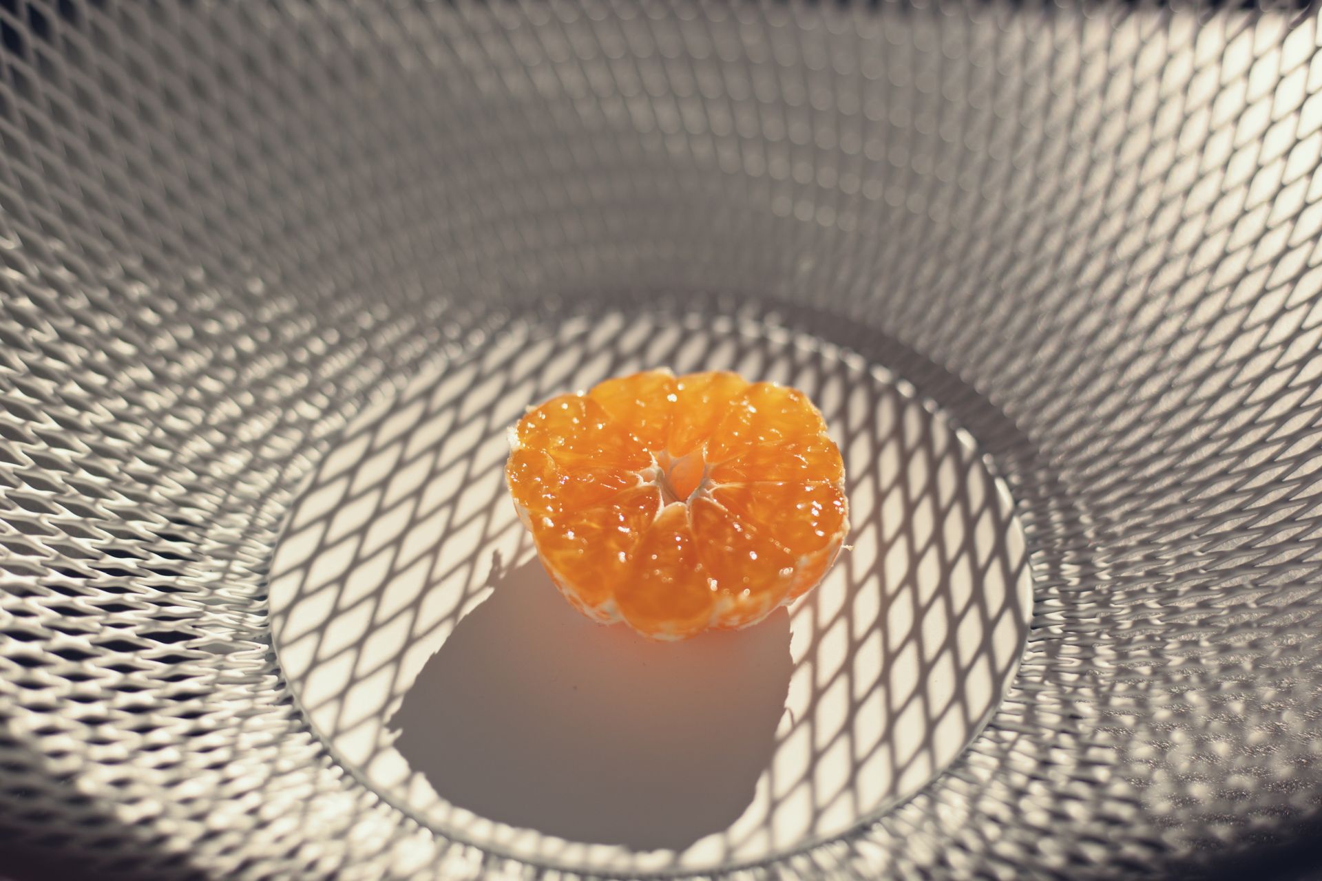 Close-up of orange slice on a mesh surface casting intricate shadows. Perfect for food and abstract themes.