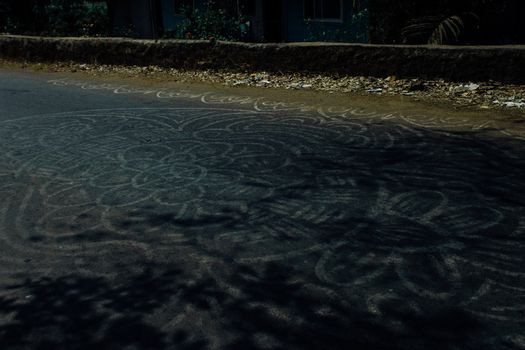 Pale white abstract mandala ornament painted on asphalt road in rural area in daylight