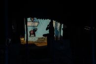 Male silhouette yawning and covering mouth with fist while sitting in dark poor shabby shelter