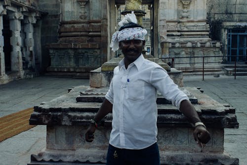 Happy Asian male in casual wear and headscarf standing with arms outstretched and looking at camera in weathered stone palace patio