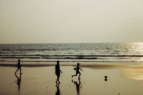 Children silhouette playing football on wet seashore at sunset