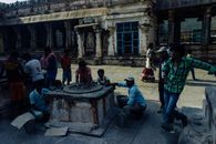 Asian people in casual clothes standing near and touching weathered religious stone wheel located in center of medieval historic Hampi village in India