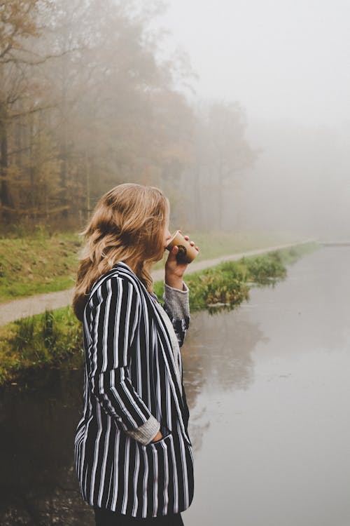 Woman Wearing a Striped Blazer Standing Beside a Lake