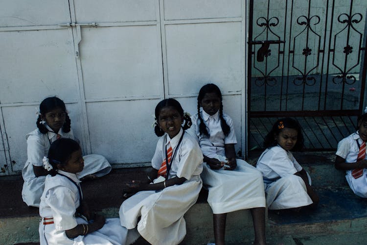 Asian Schoolgirls Resting On Ground Near School Gate