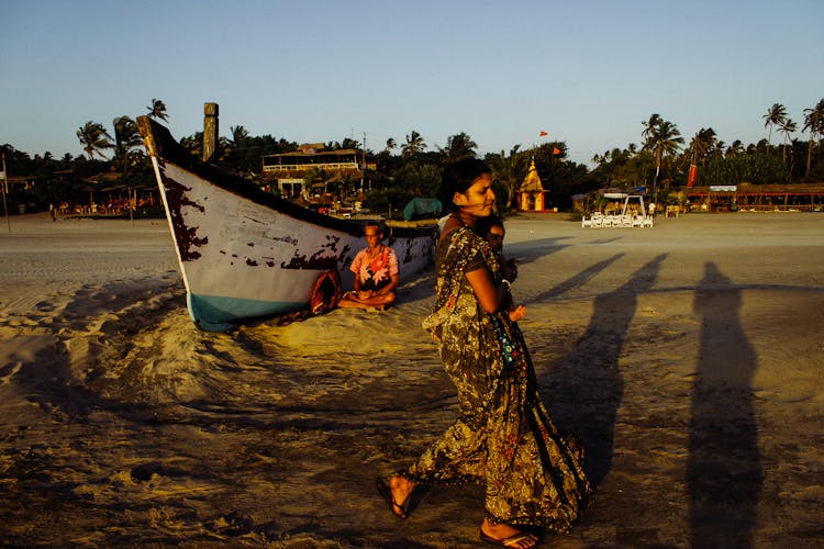 Indian Woman Carrying Baby Along Sandy Beach Near Shabby Boat