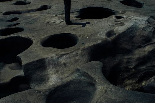 High angle of crop unrecognizable person standing on rocky uneven formations with round holes in daylight in nature