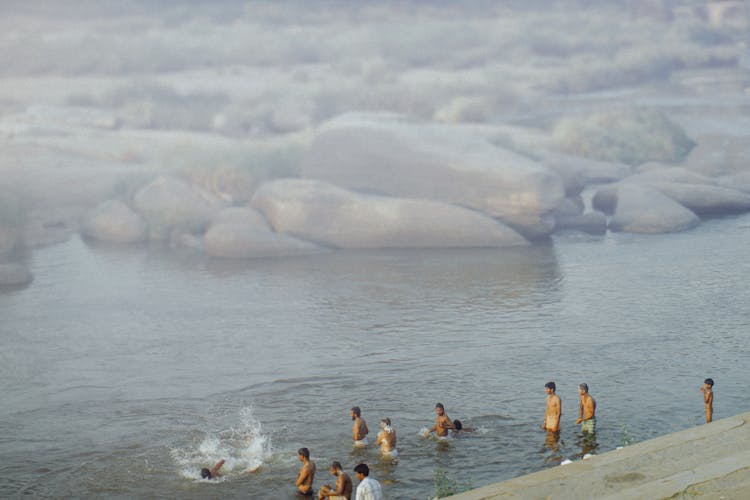 People Swimming In Sea With Stones