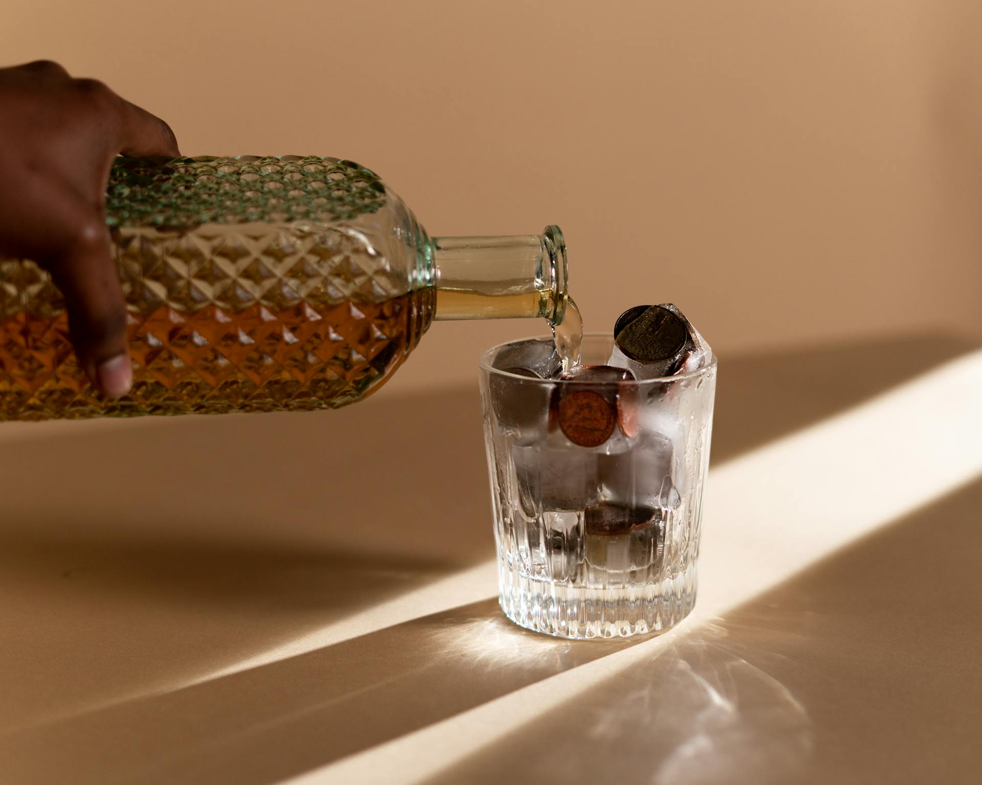 A Person Pouring Liquor in the Clear Glass with Coins