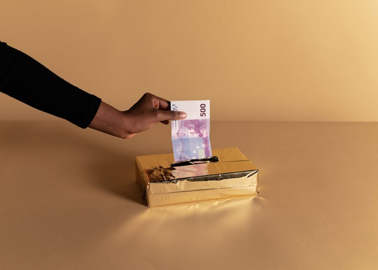 Person Putting Money Inside The Gold Box