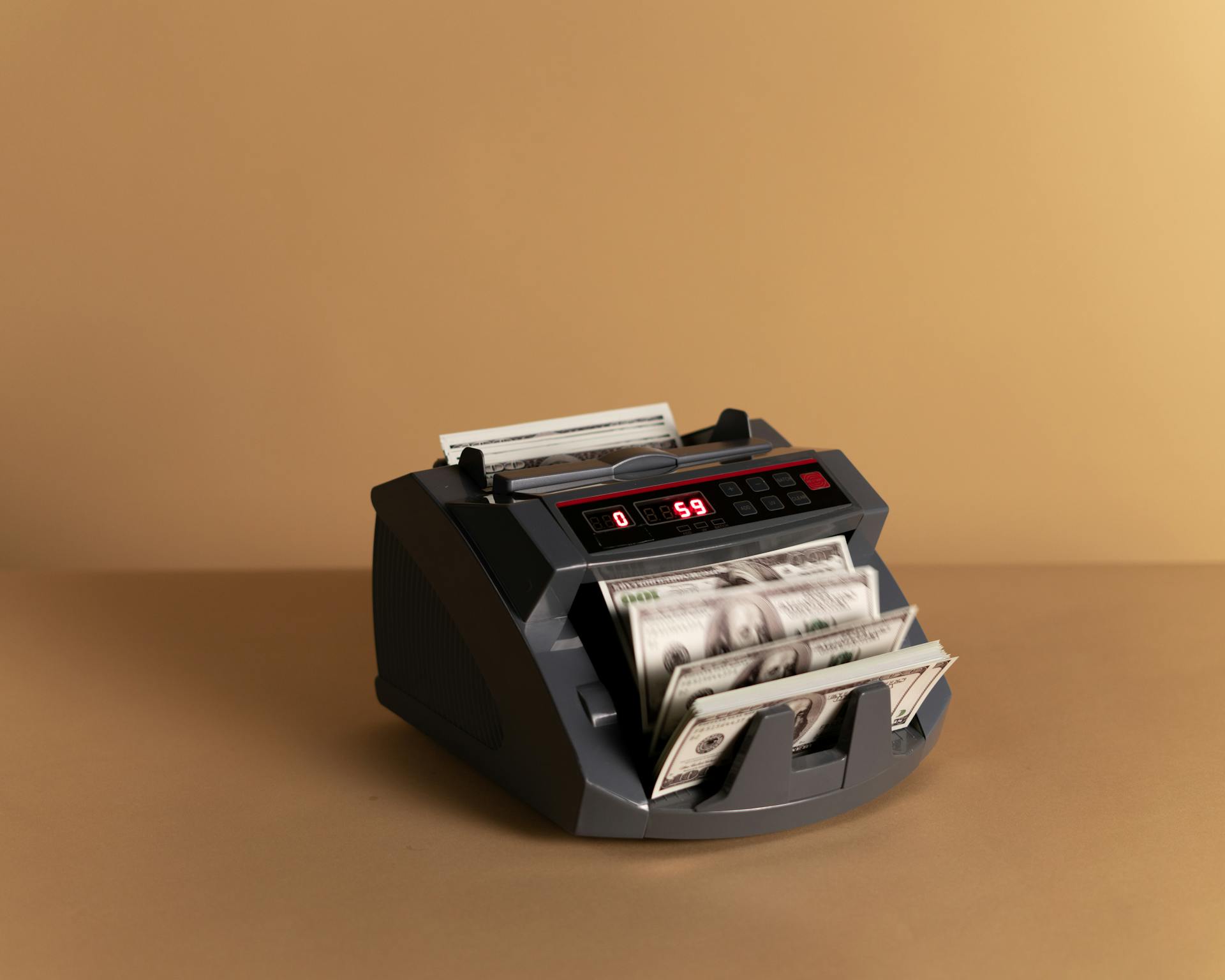 A digital money counter processing US dollars on a beige backdrop, illustrating financial concepts.