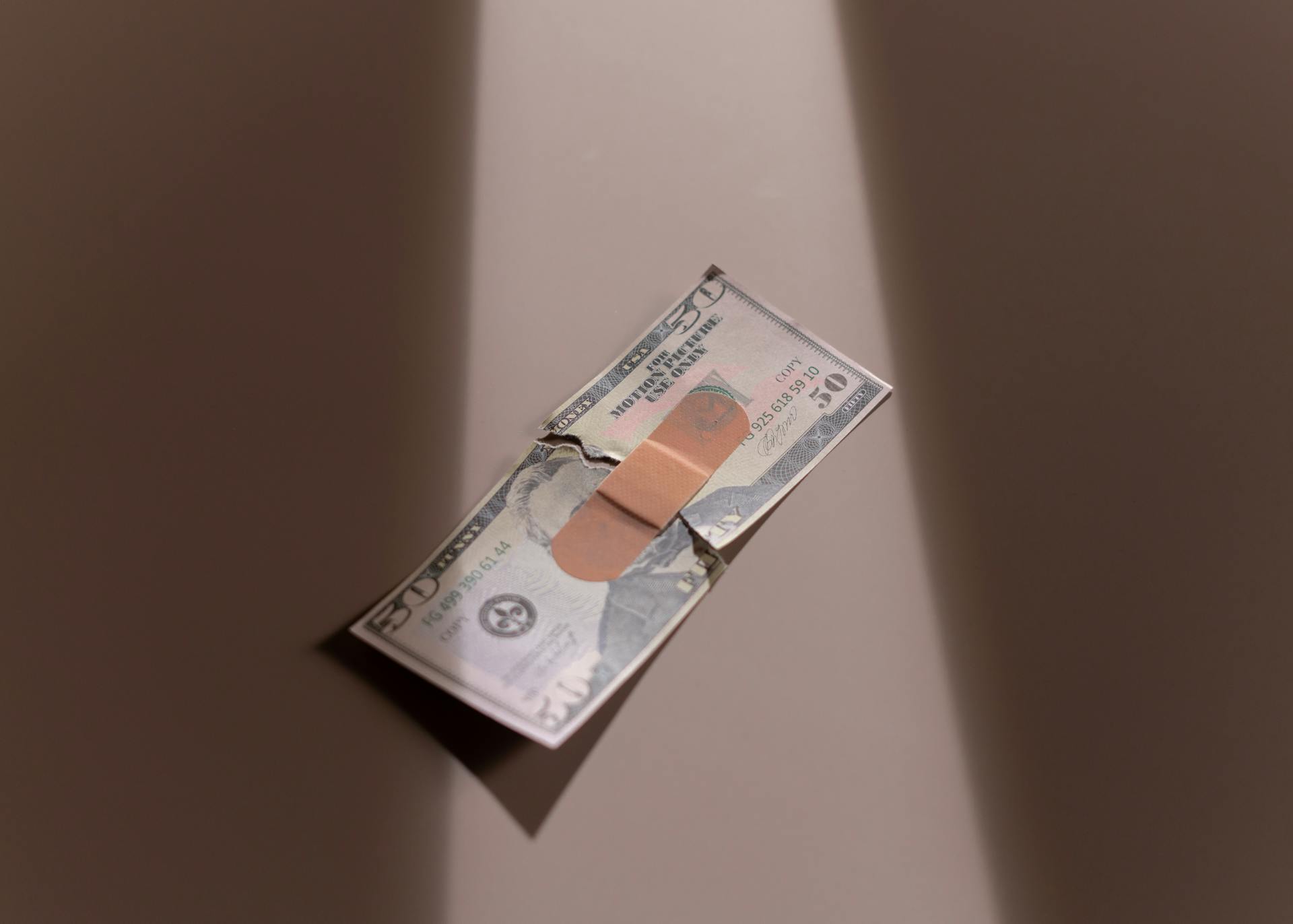 A $50 bill with a bandage symbolizes financial recovery and repair.