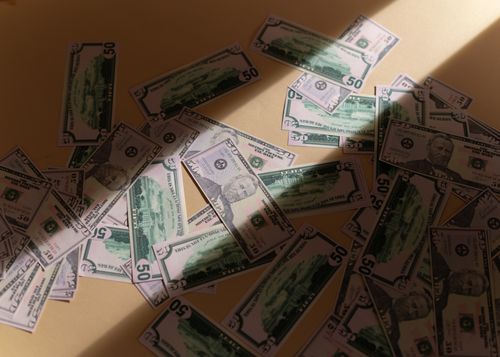 Free Scattered US dollar bills on a beige surface, creating a pattern with shadows and light. Stock Photo