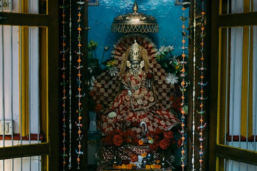 Colourful statue of Indian traditional god sculpture on throne with bright clothes decorated with flowers in traditional oriental altar for home prays and meditations