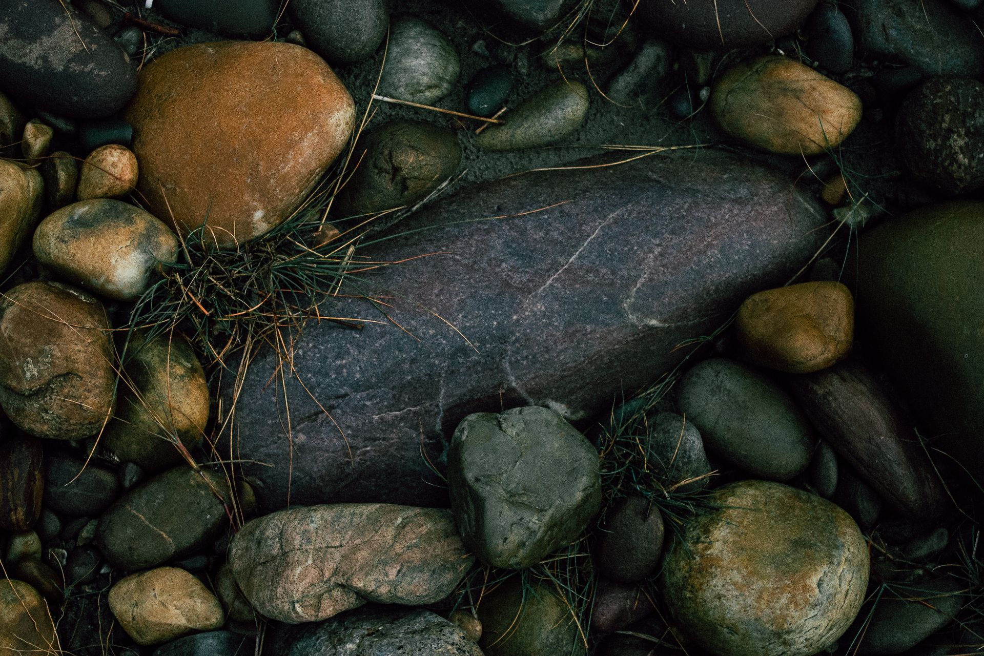 From above of rough stones of different colors covered with dry grass on ground of shore