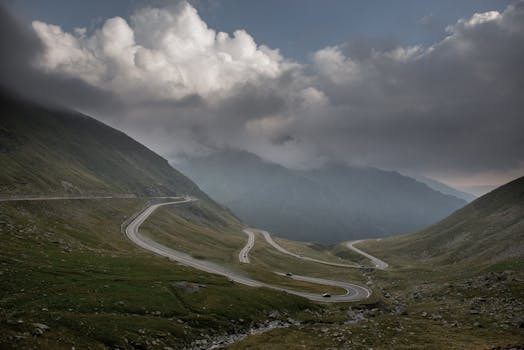 Dramatic view of a winding road in the Carpathian Mountains, Romania, under cloudy skies.