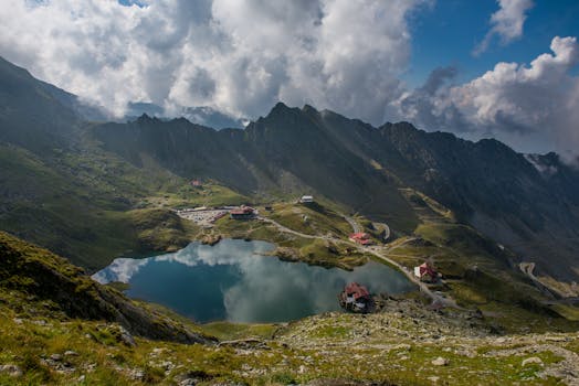 A stunning aerial view of a serene lake surrounded by majestic Romanian mountains and dramatic clouds.