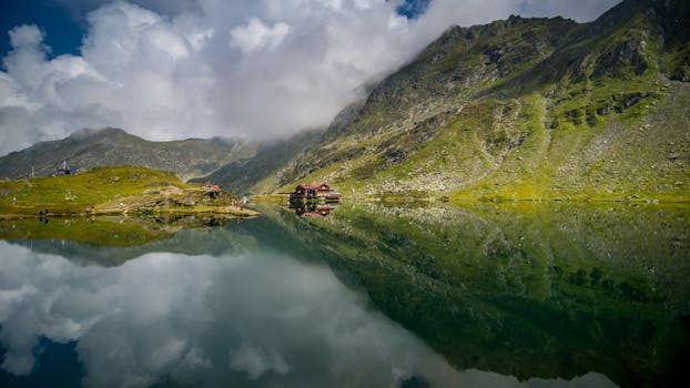 Scenic view of Bâlea Lake's reflection surrounded by majestic Făgăraș Mountains, Romania.