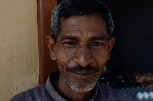 Smiling Indian man in casual clothes looking at camera while standing near entrance of house