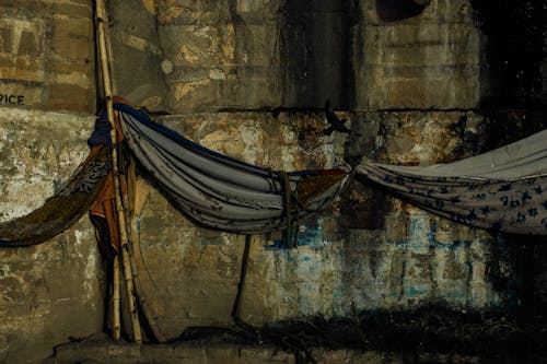 Fabric hammocks hanging on bamboo stick against aged damaged weathered wall of embankment