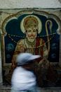 Side view of ethnic man moving past Hinduism image painted on wall in India