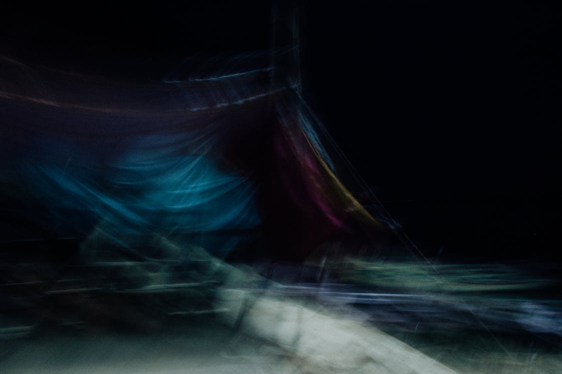 Dynamic abstract obscure background of draped bright cloth in motion hanging in darkness