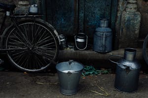 Tin vessels and metal bucket with milk placed near bike leaned on shabby rusty wall