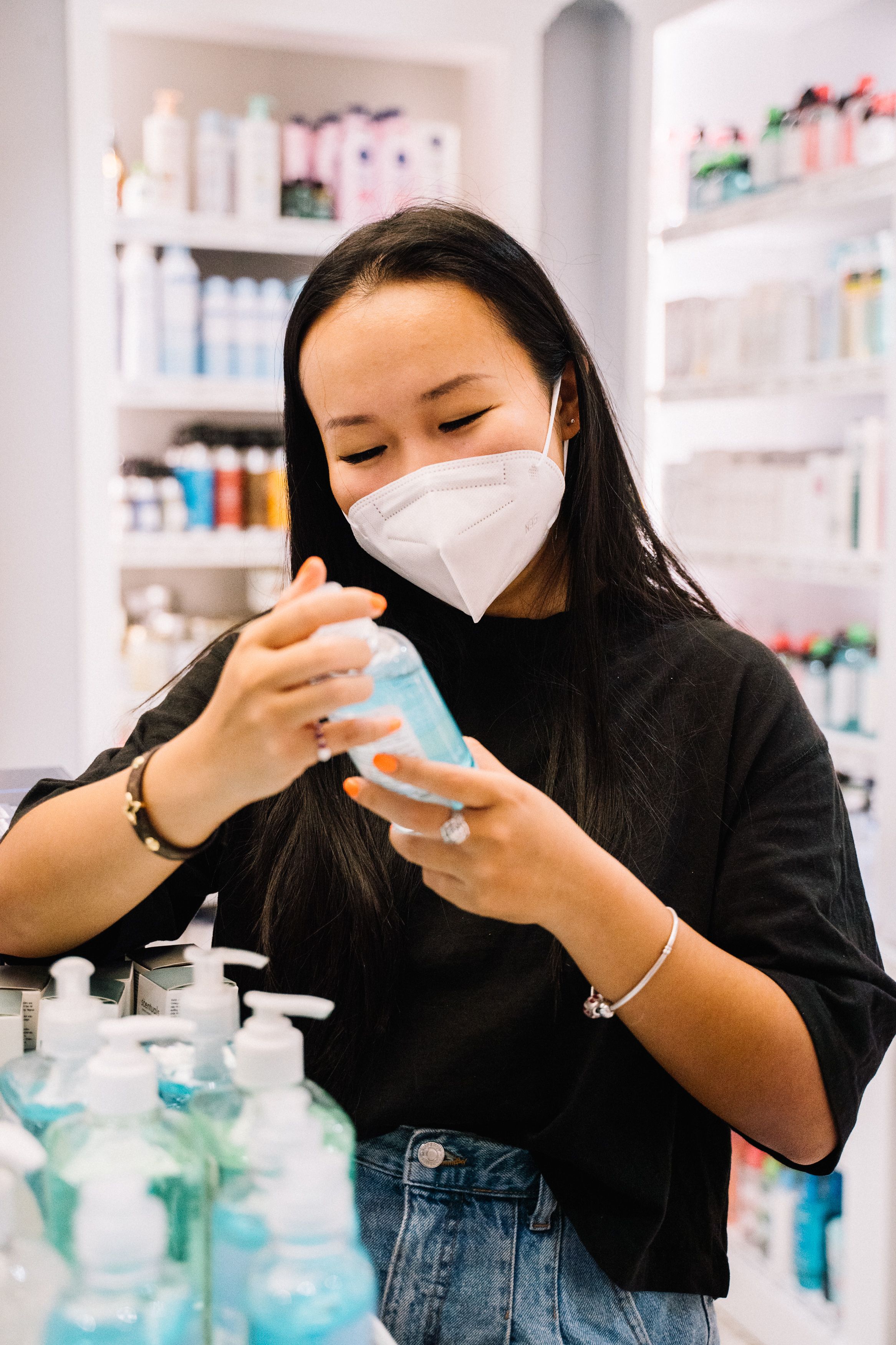 一名女子在商店里挑选洗手液，她戴着口罩，注重卫生安全