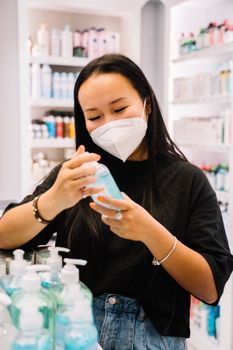 一名女子在商店里挑选洗手液，她戴着口罩，注重卫生安全