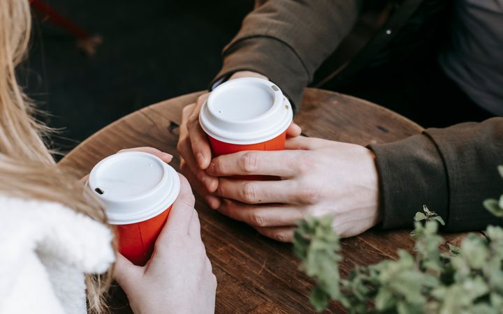 Crop faceless couple having date with takeaway beverage on wooden terrace of cafeteria